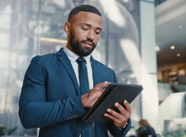 Businessman in a suit reviewing data on a tablet in a modern office lobby, representing multi-location compliance oversight.